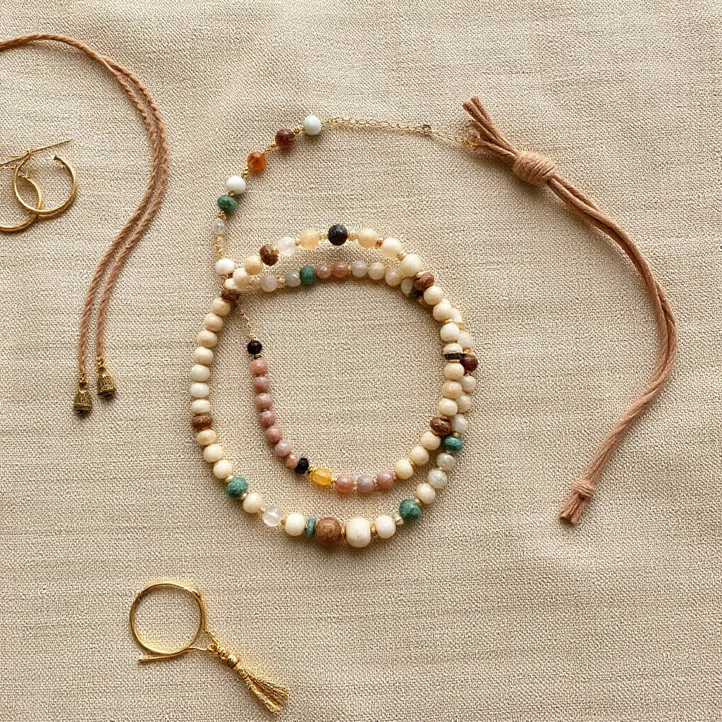 Layered bohemian-style necklaces, bracelets, and hoop earrings arranged on neutral fabric