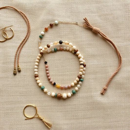 Layered bohemian-style necklaces, bracelets, and hoop earrings arranged on neutral fabric